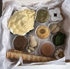 a box filled with assorted pastries on top of a white tablecloth covered floor