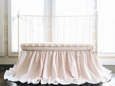 a white crib with a pink ruffled bed skirt on it's bottom