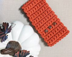 an orange crocheted cell phone case sitting on top of a white plate next to a pumpkin