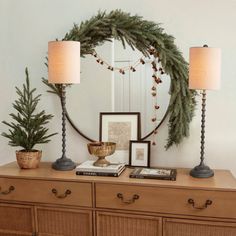 a christmas wreath on top of a dresser next to two lamps and a framed photograph