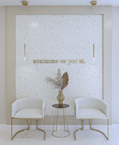 two white chairs sitting next to each other in front of a wall with gold lettering