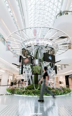 a woman is walking through an indoor shopping mall with plants and flowers on display in the center