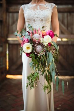 a woman holding a bouquet of flowers on her wedding day in front of a barn