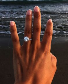 a woman's hand with a diamond ring on it near the ocean and waves