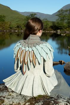 a woman sitting on top of a rock next to a body of water with wings