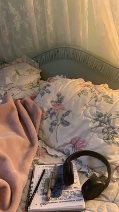 headphones, notebook and pen on a bed with floral sheets in the sunlight at night