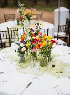 the table is set with flowers in vases and empty wine glasses for guests to drink