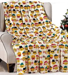 a christmas tree is next to a chair with a blanket on it and an emoticive design