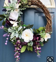 a wreath with flowers and greenery hanging on the front door to welcome people into the house