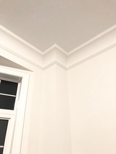 the corner of a room with a window and white paint on the walls is empty