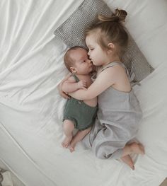 two little kids laying on top of a bed next to each other with their arms around each other