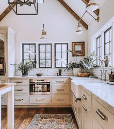 a kitchen with white cabinets and wooden floors, an area rug on the floor and two windows