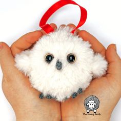 a small white stuffed animal being held by someone's hands with a red ribbon