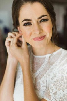 a woman wearing a white dress smiling at the camera with her hands on her chin