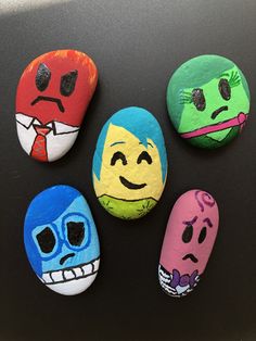 four painted rocks with faces on them sitting next to each other in front of a black surface