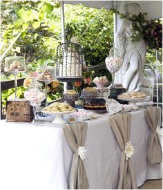 a table topped with lots of food next to a white statue in the middle of a garden