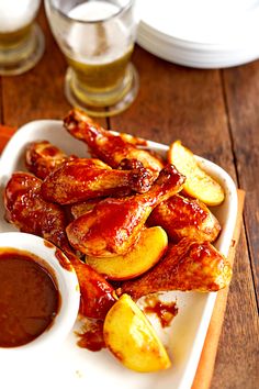 chicken wings with sauce and potatoes on a white platter next to glasses of beer