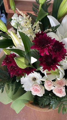 a bouquet of flowers sitting on top of a wooden table next to a vase filled with white and red flowers