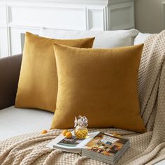 two yellow pillows sitting on top of a white couch next to a book and pineapple