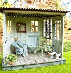 a miniature garden shed with two chairs and a table on the porch, sitting outside