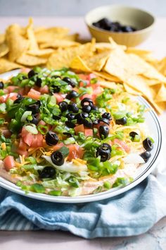 a white plate with black olives, lettuce and tomatoes on it next to tortilla chips