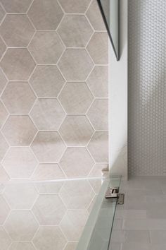 a bathroom with white tile and hexagonal tiles on the wall, along with a glass shower door