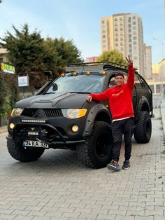 a man standing in front of a black suv with its hood up and arms raised