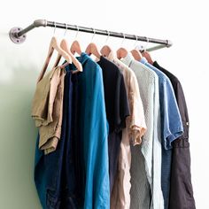 several shirts hanging on a clothes rack in front of a white wall with a coat hanger