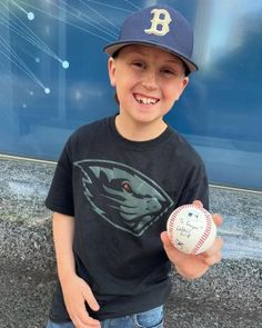 a young boy is holding a baseball in his left hand and smiling at the camera