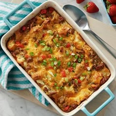 a casserole dish with meat, cheese and vegetables on a table next to strawberries