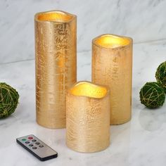 three gold candles sitting next to each other near a remote control on a marble surface