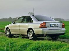 a silver car parked on the side of a dirt road next to a green field