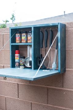 a blue shelf with utensils hanging from it's sides on a brick wall