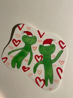 two green teddy bears wearing santa hats on top of a white table with red hearts