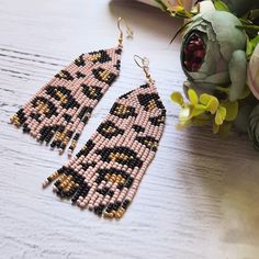 a pair of beaded earrings sitting on top of a wooden table next to flowers