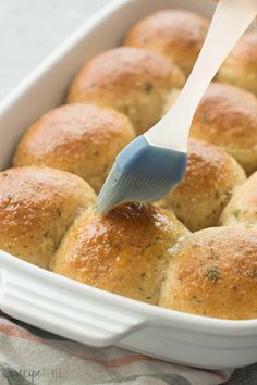 someone using a spatula to dip something in a casserole dish filled with rolls