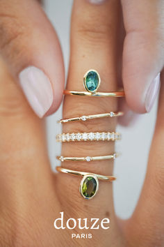 a woman's hand with five different rings on her fingers and one is holding an emerald