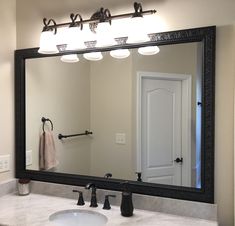 a bathroom sink with a large mirror and lights on the wall above it's faucet