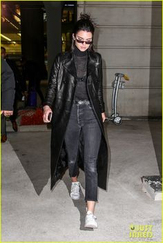 a woman in black jacket and jeans walking through an airport