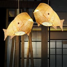 two fish lamps hanging from the ceiling in a room with bamboo poles and windows behind them