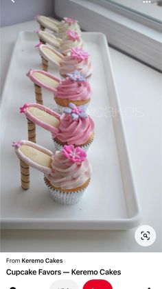 cupcakes with pink frosting and bows are lined up on a white tray