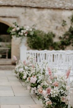 rows of white and pink flowers lined up along the side of a stone wall next to a brick building