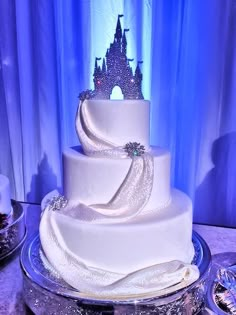 a white wedding cake with a castle on top is sitting in front of a blue curtain