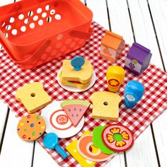 a red plastic basket filled with toys on top of a checkered tablecloth covered floor