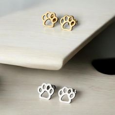 two pairs of earrings with paw prints sitting on top of a white table next to a computer keyboard