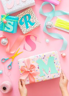 a person holding a gift box with ribbon and other items surrounding it on a pink background