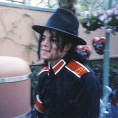 a young man wearing a black hat and jacket standing next to a pink trash can