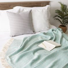 a bed with pillows and a blanket on it, next to a potted plant