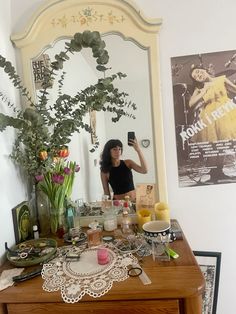 a woman taking a selfie in front of a mirror with flowers on the dresser