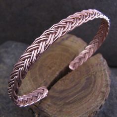 a pink gold braided ring sitting on top of a piece of wood